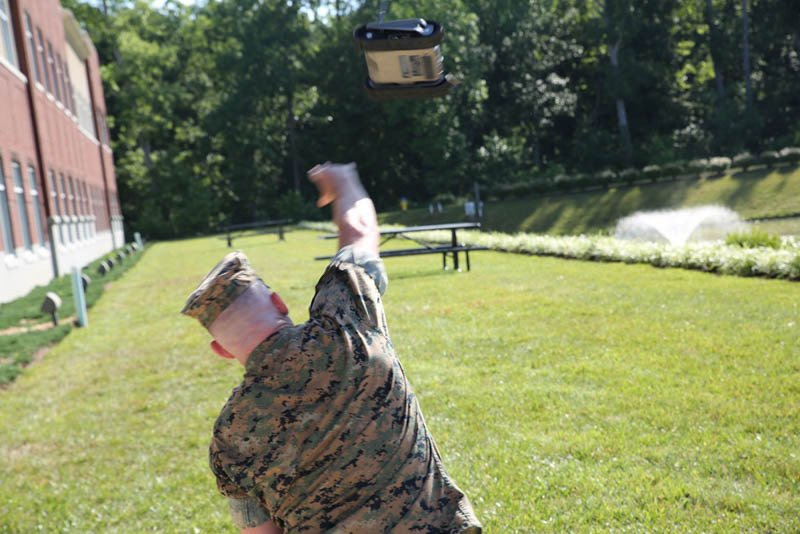 A U.S. Marine throws a small robust wheeled robot across a grassy field