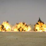 three large military munition explosions clustered in a row on a desert backdrop