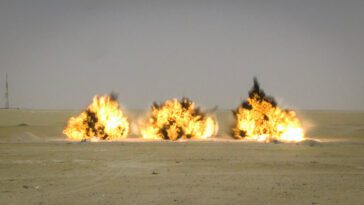 three large military munition explosions clustered in a row on a desert backdrop