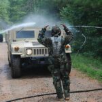 Soldiers in camouflage spray down military vehicles lined up on a road